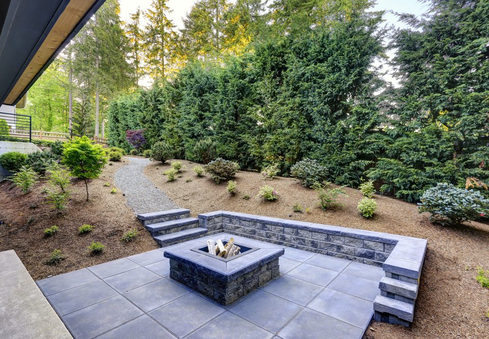 New modern home features a backyard with rectangular concrete fire pit framed by slate pavers and overlooking the lush garden. Northwest, USA