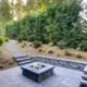 New modern home features a backyard with rectangular concrete fire pit framed by slate pavers and overlooking the lush garden. Northwest, USA