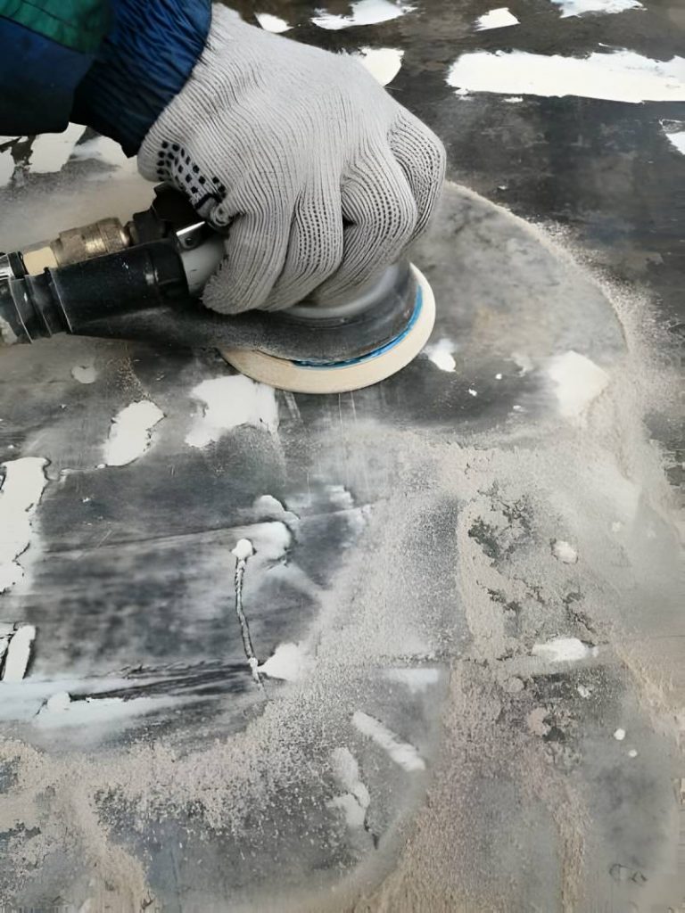 Work with a pneumatic orbital machine in a hand in a white glove on a dark putty surface