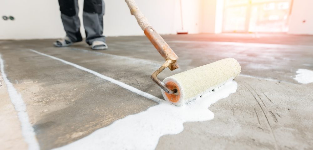 Closeup floor priming process with sun light. Worker use primer on concrete floor before leveling, strengthening surface.