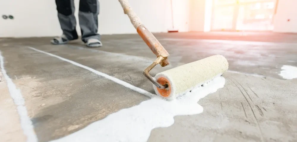 Closeup floor priming process with sun light. Worker use primer on concrete floor before leveling, strengthening surface.