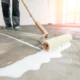 Closeup floor priming process with sun light. Worker use primer on concrete floor before leveling, strengthening surface.