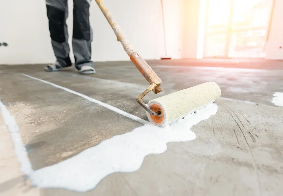 Closeup floor priming process with sun light. Worker use primer on concrete floor before leveling, strengthening surface.