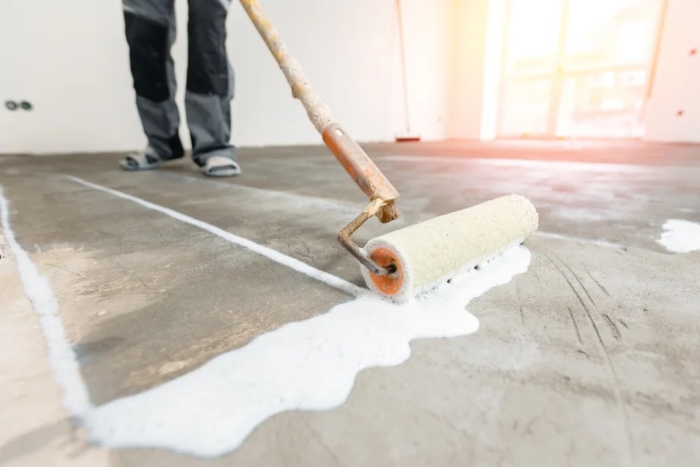 Closeup floor priming process with sun light. Worker use primer on concrete floor before leveling, strengthening surface.