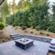 New modern home features a backyard with rectangular concrete fire pit framed by slate pavers and overlooking the lush garden. Northwest, USA